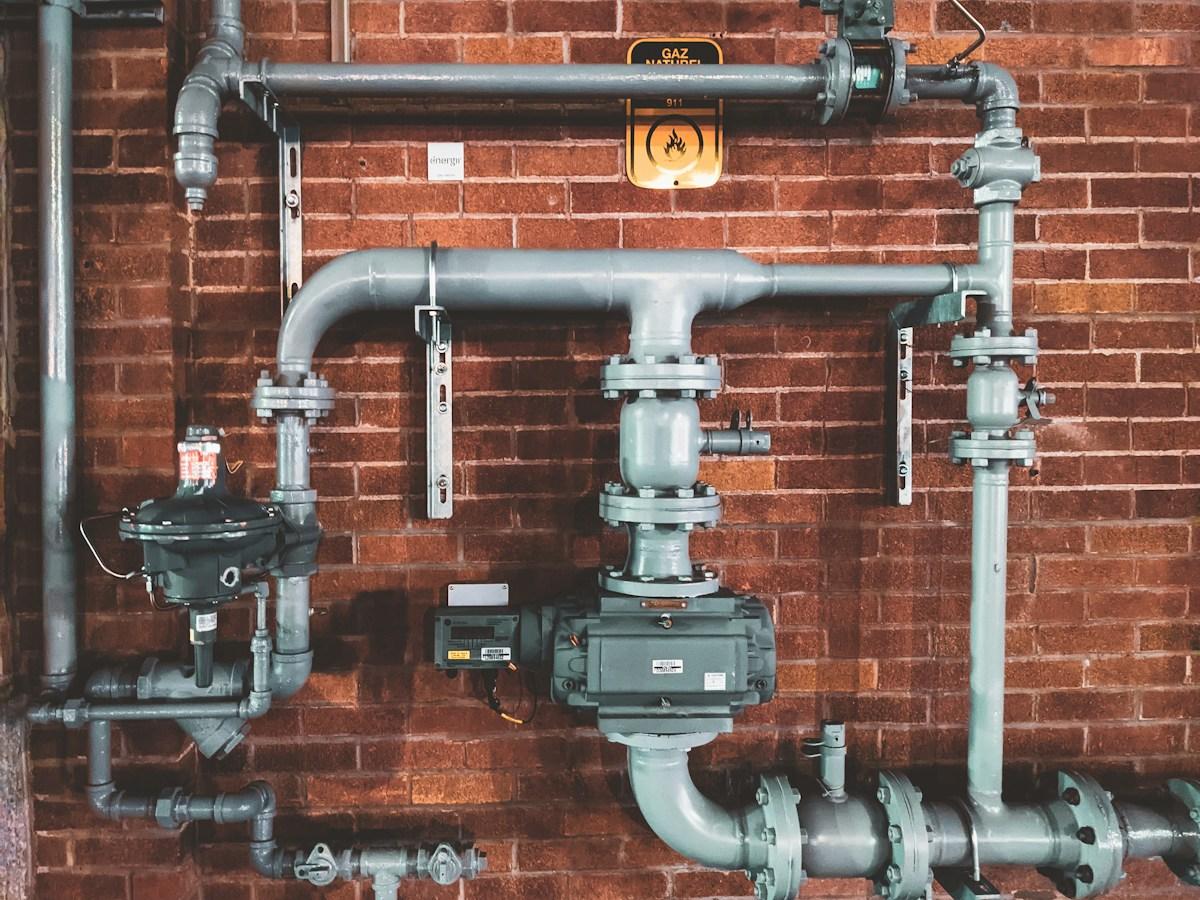 Professional mechanical piping and valves mounted on a brick basement wall, illustrating the kind of utility work involved in soil-gas venting systems